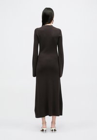 Długa brązowa sukienka max z dzianiny, z długimi rękawami, dopasowanym krojem i dekoltem w serek. Gładka tekstura i subtelne przeszycia z tyłu.