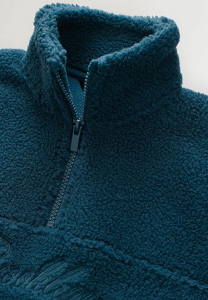Dark teal fleece pullover with textured fabric, a half-zipper closure, and embroidered text on the chest area.