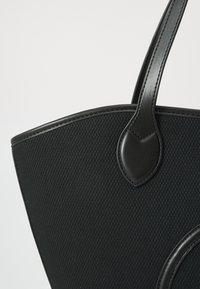 Borsa tote nera con tessuto strutturato e dettagli in pelle liscia, dalla forma strutturata e con una parte superiore arrotondata. I manici sono eleganti e robusti.