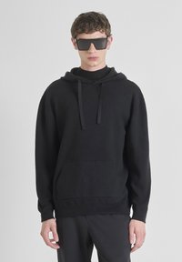 Felpa con cappuccio nera realizzata in tessuto morbido, con tasca frontale, maniche lunghe e vestibilità comoda. Indossata con occhiali da sole neri oversize.