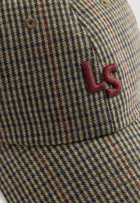 Casquette à motif pied-de-coq en vert olive avec des rayures rouges et bleu marine. Présente un logo "LS" brodé en bourgogne. Tissu texturé, forme structurée.