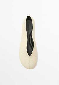 Scarpa piatta beige con una morbida texture, design minimale e apertura a forma di mandorla. Soletta nera visibile all'interno della scarpa.