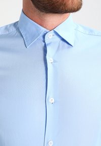 Ljusblå knäppskjorta med en mjuk textur, klassisk krage och vita knappar, med en strömlinjeformad design och slätt tyg.