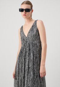 Robe sans manches à motif noir et blanc avec un décolleté en V profond, en tissu texturé, au design fluide, accompagnée de lunettes de soleil carrées.