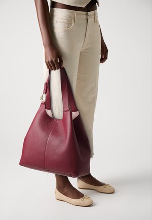 Large, burgundy leather tote bag with a textured surface and soft, slouchy silhouette. Features contrasting cream accents and a gold hardware detail.