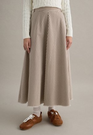 Una falda larga y fluida con rayas diagonales marrones y blancas, con una pretina alta, combinada con zapatos marrón claro y calcetas blancas.