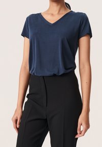 Námořnické modré tričko s výstřihem do V vyrobené z měkké látky, krátké rukávy, volný střih, spárováno s černými úzkými kalhotami. Hladká textura, minimalistický design.