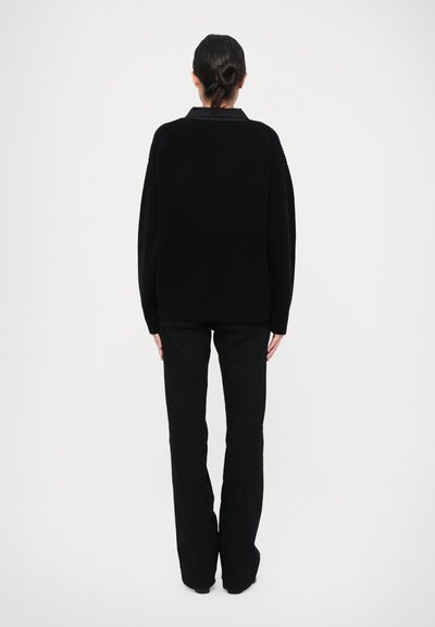 Black oversized knit sweater with a crew neckline, textured fabric, and dropped shoulders; paired with black fitted pants, shown from behind.