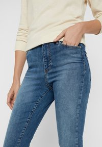 Jeans de denim azul ajustados con un diseño de cinco bolsillos, cintura de altura media y sutiles detalles de costura. Textura suave y corte clásico.