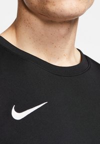 Zwarte Nike t-shirt met een ronde hals, korte mouwen en een wit swoosh-logo aan de linkerkant. Zachte stoftextuur.