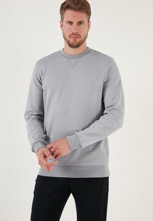Lichtgrijze sweatshirt met een gestructureerde afwerking, ronde hals, lange mouwen en ribgebreide manchetten, gedragen met donkere broek. Geen zichtbare logo's.
