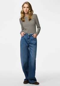 Top a maniche lunghe a righe in bianco e nero, abbinato a jeans in denim blu a gamba larga. Dettagli usurati e design tradizionale a cinque tasche.