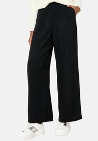 Black, wide-leg pants made of soft fabric, featuring a high waist and side pockets, paired with white sneakers with metallic accents.