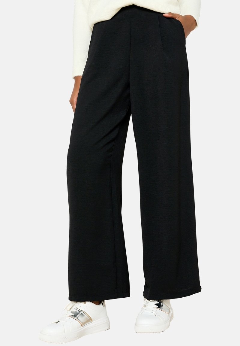 Black, wide-leg pants made of soft fabric, featuring a high waist and side pockets, paired with white sneakers with metallic accents.