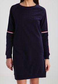 Navyblaues Sweatshirtkleid mit langen RaglansÄrmel, ausgestattet mit roten und weißen Streifen entlang der Ärmel, glatter Textur und Rundhalsausschnitt.
