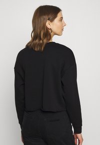 Sweatshirt preto cropped com um corte descontraído, apresentando mangas longas e um decote redondo, combinado com calças pretas de cintura alta.