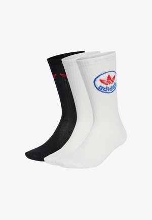 Set de chaussettes Adidas, noir et blanc. Texture côtelée, longueur mi-mollet. Logo rouge sur la paire noire, logo bleu sur un patch circulaire de la paire blanche.