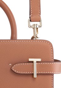 Borsa a mano in pelle tan con forma strutturata, hardware dorato, cuciture a contrasto e un accento decorativo a forma di 'T' sulla tracolla frontale.