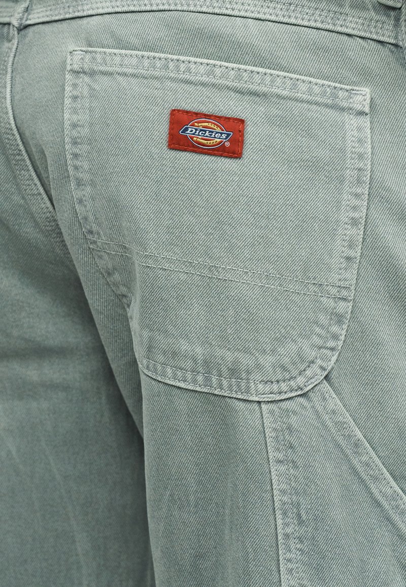 Lichtgrijze spijkerbroek met een achterzak met een rood Dickies-logo. Gestructureerde stof met zichtbare stiksel details.