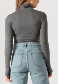 Grijze langetermijn turtleneck top gecombineerd met lichtblauwe hoge taille denim jeans met twee achterzakken en een licht vervaagde textuur.