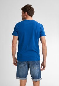 Modré bavlněné tričko s krátkými rukávy, kulatým výstřihem a volným střihem, doplněné džínovými šortkami s ohrnutými manžetami a zadními kapsami.