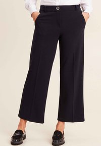 Zwarte wijde broek met een gladde textuur, voorzien van zijzakken en een sluiting met een knoop aan de voorkant. Gemaakt van een lichte stof.