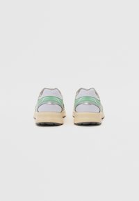 Sportskor med en grå mesh-överkonstruktion, gröna accentdetaljer och en beigefärgad gummisob. Har en vadderad krage och en strukturerad sula för bra grepp.