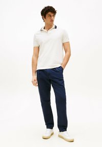 Polo bianco con colletto blu navy, abbinato a pantaloni blu scuro e sneakers bianche. Vestibilità slim e texture morbida, stile casual.