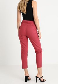 Pantalons tailleur roses à coupe slim, longueur cropped et tissu lisse. Dotés d'une taille avec passants de ceinture et de poches latérales.