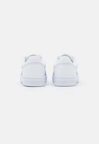 Weiße Sportschuhe mit einem glatten, synthetischen Obermaterial, gepolstertem Knöchelkragen und einer Gummisohle mit horizontalen Rillen für besseren Halt.
