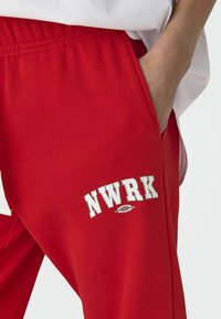 Røde sweatpants lavet af en bomuldsblanding med et broderet logo "NWRK" og en sidelomme samt en elastisk talje.