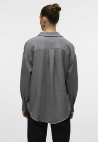 Gray oversized shirt with a textured surface, a collar, and buttoned cuffs, featuring a pleated design along the back.