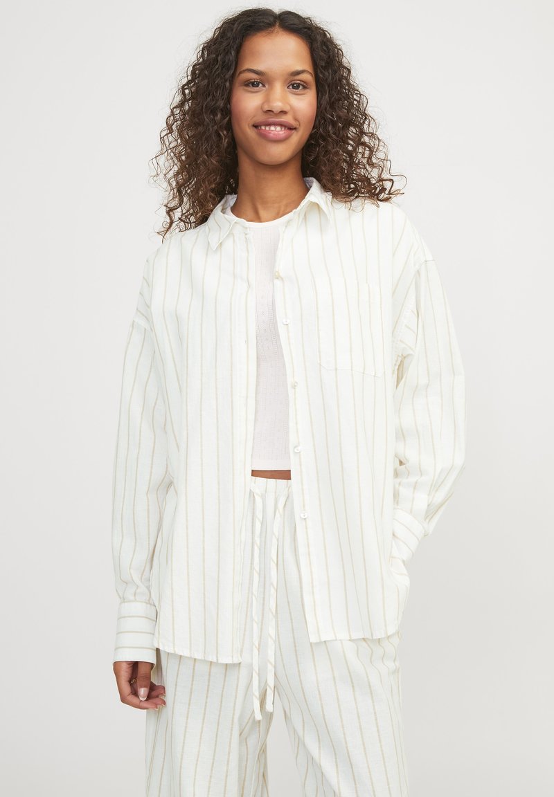 Camisa de botones blanca a rayas con mangas largas y un bolsillo, combinada con pantalones ligeros a juego que tienen una cintura con cordón.