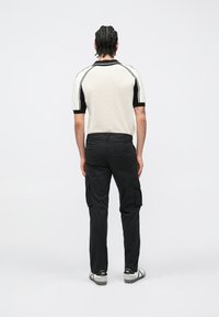 Πλεκτό πόλο πουκάμισο ανδρών με κοντό μανίκι σε κρεμ και μαύρο, με εφαρμοστή γραμμή, συνδυασμένο με μαύρο παντελόνι cargo με τσέπες στο πλάι και ίσια εφαρμογή.