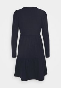 Robe noire à manches longues avec épaules bouffantes froncées, taille cintrée et jupe évasée à volants, vue de dos sur un fond blanc.