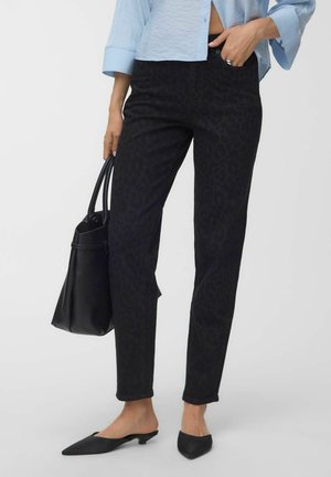 Femme portant un pantalon noir slim avec un imprimé animal discret, une chemise courte bleu clair, des chaussures noires pointues à petit talon, et portant un sac à main noir.