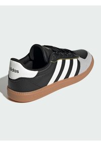 Čierne a šedé tenisky s bielymi pruhmi, textúrovanou gumovou podrážkou a klasickým brandingom Adidas. Majú šnurovací dizajn a vypchávku okolo goliera.