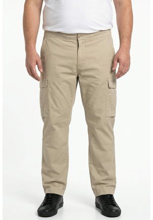 Mann trägt beige Cargohosen mit Seitentaschen und schwarze Schnürschuhe, steht vor weißem Hintergrund.