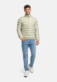 Lys grøn puffjakke med vandret syninger, høj krave og lynlås, parret med lyseblå jeans og hvide sneakers.