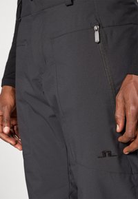 Černé voděodolné kalhoty s kapsou na zip, hladkým povrchem, tapered designem a logem na stehně.