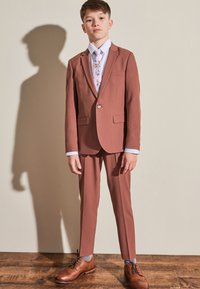 Brown suit with a slim fit design, featuring a single button jacket, paired with a white shirt and a light-patterned tie. Brown shoes.