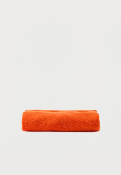 Serviette orange vif pliée posée sur une surface blanche contre un fond blanc uni.