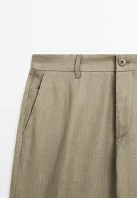 Khaki kalhoty s rovný střih, vyrobené z texturovaného materiálu. Mají zapínání na knoflík, poutka na opasek a boční kapsy.