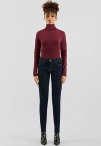 Vínový rolák v kombinácii s tmavomodrými úzkymi džínsami. Oblečenie má priliehavý strih a dopĺňajú ho špicaté čierne podpätky.