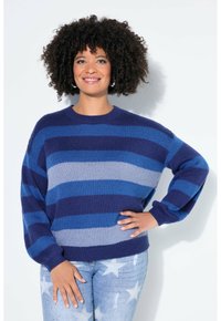 Maglione lavorato a maglia oversize a righe blu navy, blu e grigio. Presenta una scollatura rotonda e maniche larghe. Abbinato a jeans con fantasia a stelle.