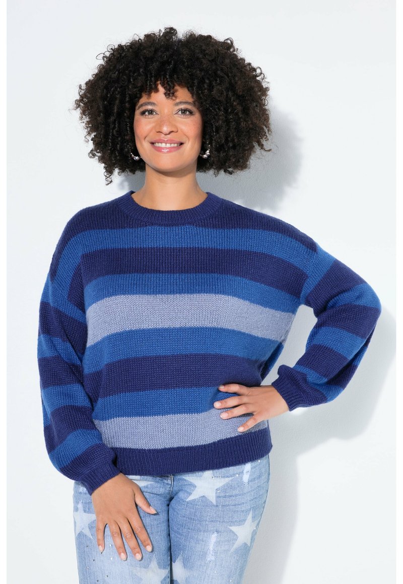 Maglione lavorato a maglia oversize a righe blu navy, blu e grigio. Presenta una scollatura rotonda e maniche larghe. Abbinato a jeans con fantasia a stelle.