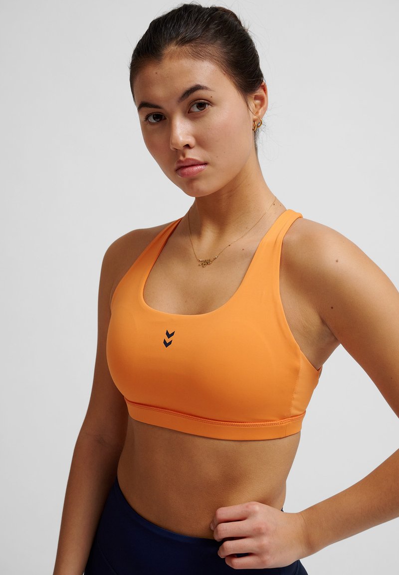 Oranje sport-bh van rekbaar materiaal met een ronde halslijn, voorzien van drie marineblauwe chevrons aan de voorkant en een aansluitend ontwerp.
