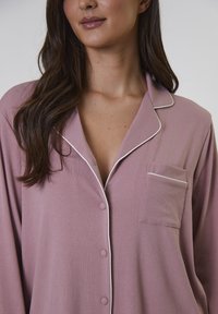 Ljusrosa ribbad pyjamasöverdel med notchkraös, långa ärmar, framficka med vit piping och knäppningar.