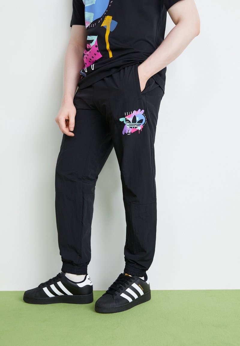 Černé teplákové kalhoty z lehkého materiálu s barevným grafickým akcentem na stehně. Kombinovány s černo-bílými teniskami.