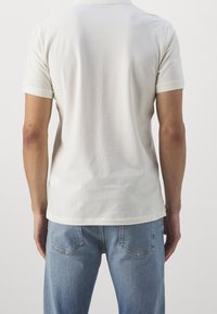 Vit bomulls-t-shirt med rund hals och korta ärmar. Bakvyn visar en jämn textur och standardpassform. Matchad med ljusblå jeans.